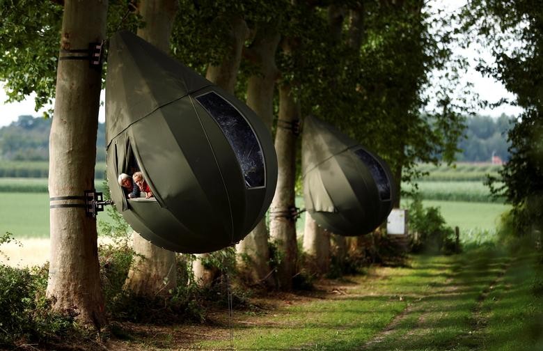Guests pose a they sit inside a teardrop-shaped tent hanging from a tree created by Dutch artist Dre Wapenaar, offering an unusual accommodation for tourists in the Belgian countryside, near Borgloon, Belgium. REUTERS/Francois Lenoir  